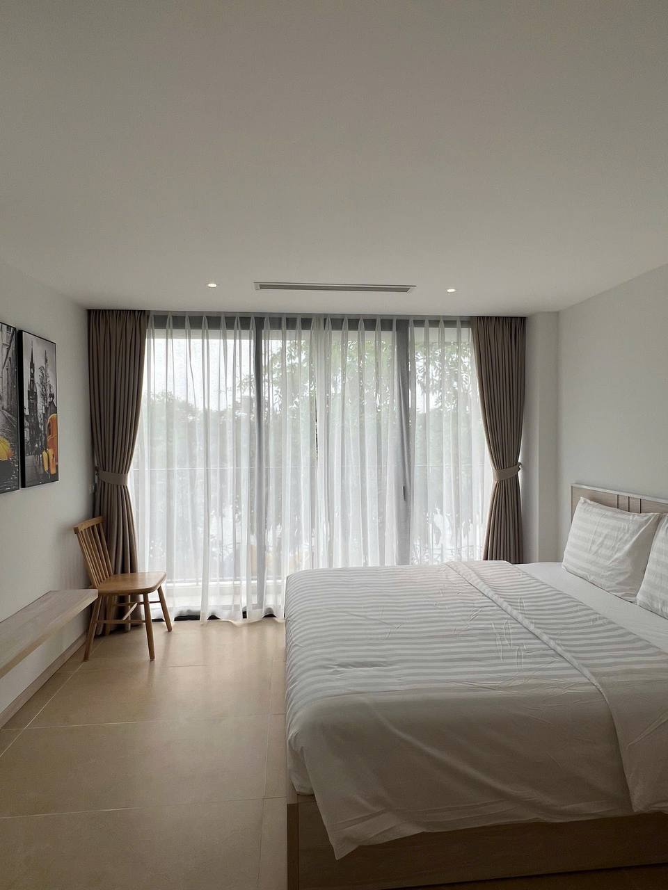 Toàn cảnh studio homestay - giường, bàn ăn với hoa đỏ, bếp mini, cửa kính lớn, ánh sáng tự nhiên