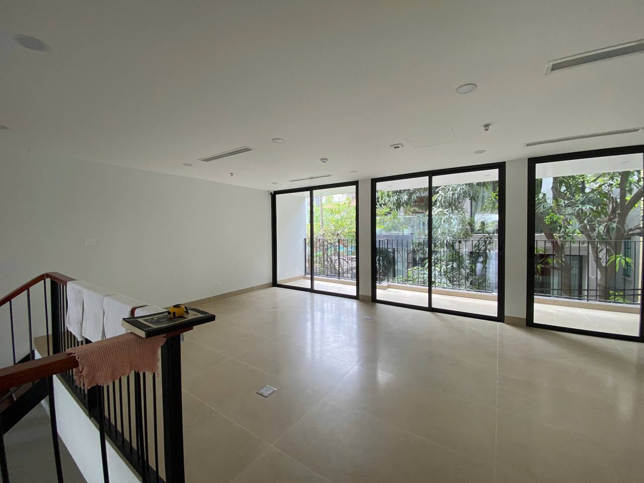 Mặt sàn trống nhìn từ cầu thang - cửa kính sliding lớn, view cây xanh, mặt bằng rộng thoáng